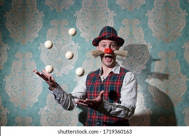 young man in a clown costume juggles on a green background false mustache and red nose, plaid vest