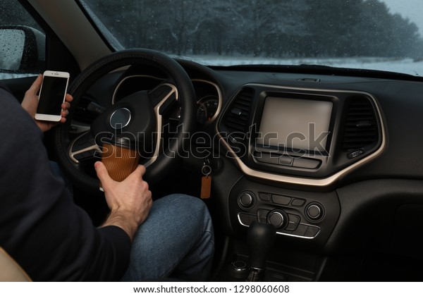 Young\
man with coffee and smartphone inside car,\
closeup