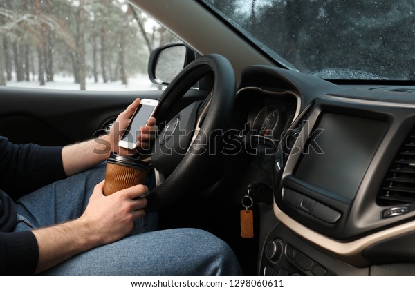 Young\
man with coffee and smartphone inside car,\
closeup