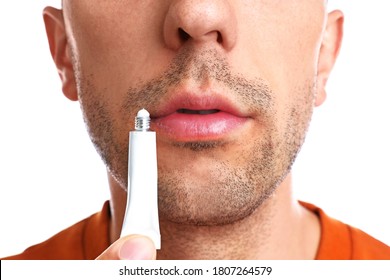 Young Man With Cold Sore Applying Cream On Lips Against White Background, Closeup