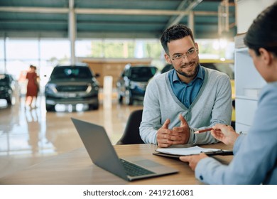 Young man communicating with saleswoman while about to sing a contract for buying new car in showroom.  - Powered by Shutterstock