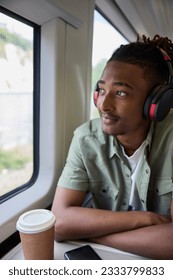Young Man Commuting To Work Sitting  On Train Wearing Wireless Headphones Looking Out Of Window