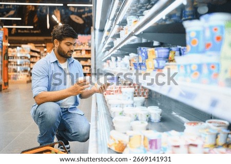 Young man comparing yogurts while crouching in the refrigerated dairy aisle of a grocery store