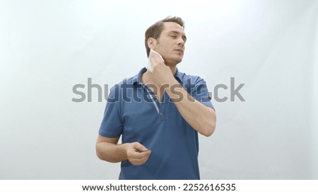 Young man complaining about summer heat isolated on white background. Angry man wiping sweat with napkin in hot weather. Stress, sweating, heat problem in summer weather.