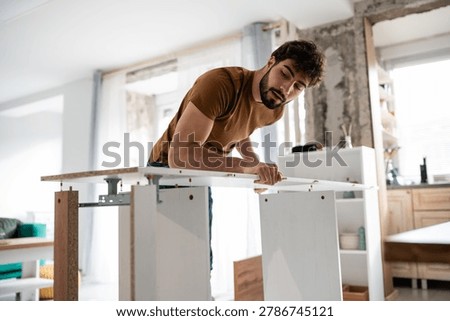 Young man concentrating on assembling new flat-pack furniture at home. Focused male builder performing diy task