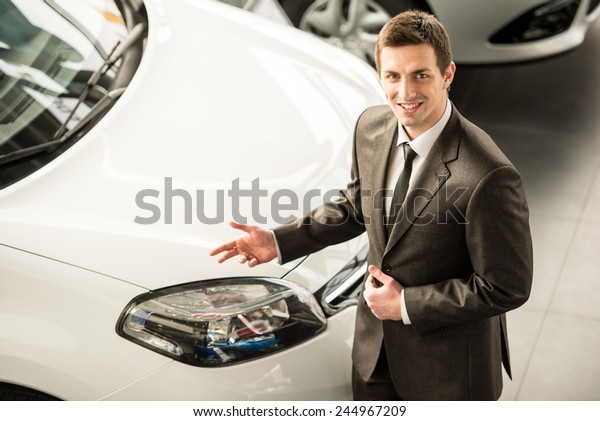 Young man consultant in showroom is standing near\
car. Top view.
