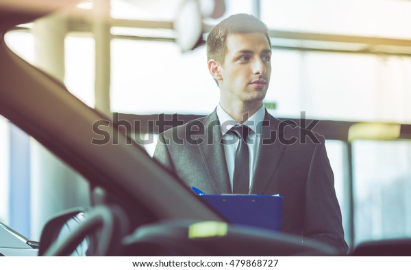 Young\
man consultant in showroom is standing near\
car.