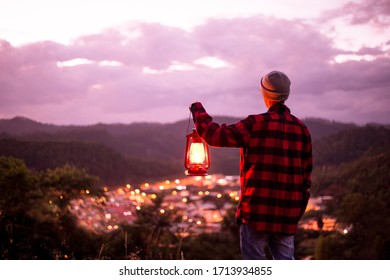 Young man contemplating the city lights with a kerosene lamp lit.  Faith and religiosity. People in night scenery. twilight sky - Powered by Shutterstock