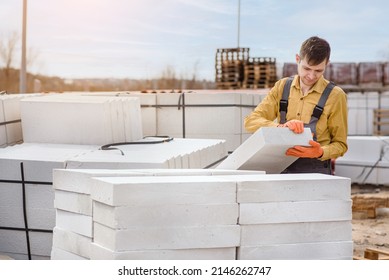 Young man contractor builder is holding an autoclaved aerated concrete block aac on a construction site.