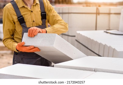 Young man contractor builder is holding an autoclaved aerated concrete block aac on a construction site. - Shutterstock ID 2172043257