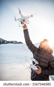 Young man controlling his drone in snowy outdoors. Drone operator holding a transmitter and landing with a drone.