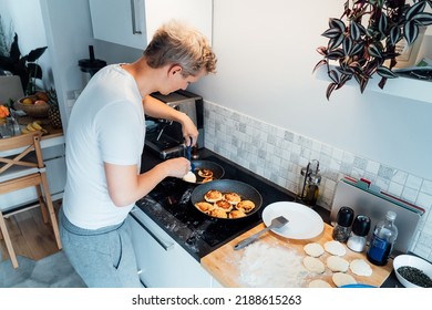 A Young Man Is Cooking Cheese Pancakes In A Modern Light Kitchen At Home. Man Preparing Pancakes For Frying On The Pan. Housework And Home Duties. Culinary Hobby.High View. Selective Focus.