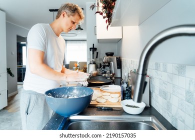 A Young Man Is Cooking Cheese Pancakes In A Modern Light Kitchen At Home. Man Preparing Pancakes For Frying On The Pan. Housework And Home Duties. Culinary Hobby. Selective Focus