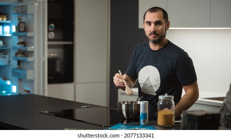 Young Man Is Cooking Dinner Or A Meal In A Fancy Big Kitchen. Hipster Guy Cooking In A White Kitchen.