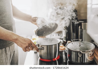 Young Man Cooking Fresh Food At Home And Opening Lid Of Steaming Pot. 