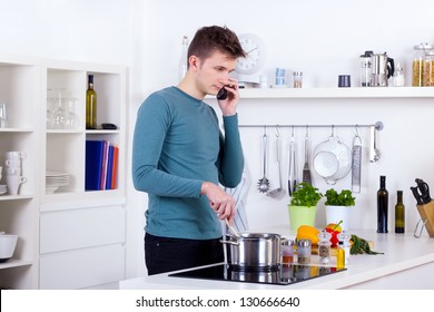 Young Man Cooking A Meal And Talking On The Phone In His Kitchen