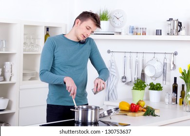 Young Man Cooking A Meal And Talking On The Phone In His Kitchen