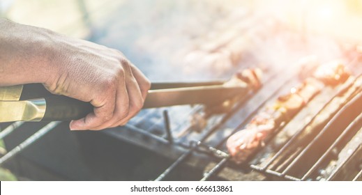 Young man cooking meat on barbecue at home in backyard - Chef putting some meat skewers on grill in park outdoor - Summer, food concept - Focus on center hand - Vintage retro filter