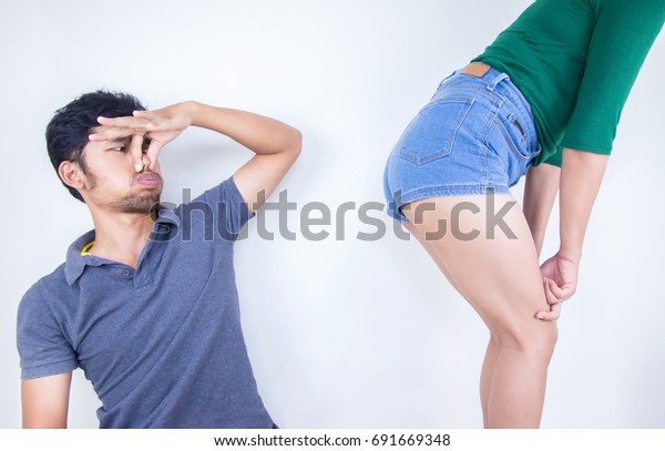 Young man\
covers him nose because of woman farting make a bad smell, Young\
man looking at her and covering him\
nose.