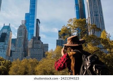 Young man in cowboy hat photographing Manhattan skyscrapers in Central Park, NYC - Powered by Shutterstock