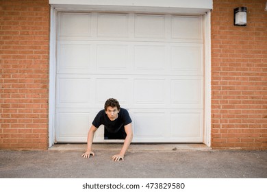 Young Man Crawling Through Hole In Garage Door