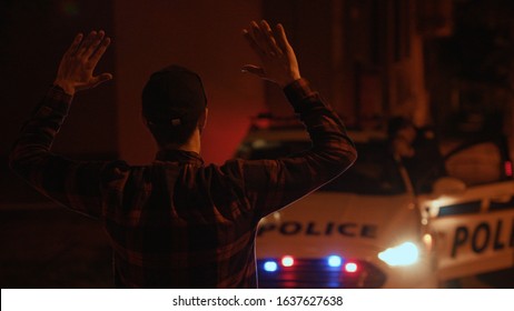 Young man criminal raises and puts hands behind his head surrenders to the police. Portrait of stressed male offender turning standing waiting for the arrest.