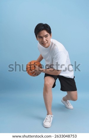 A young man crouches while preparing to dribble a basketball. He is wearing a white t-shirt and black shorts, showcasing an athletic stance against a soft blue backdrop.