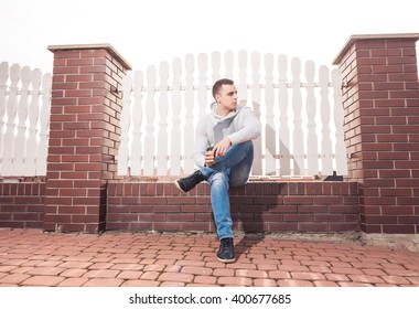 young man with cup of coffee sitting at street fence