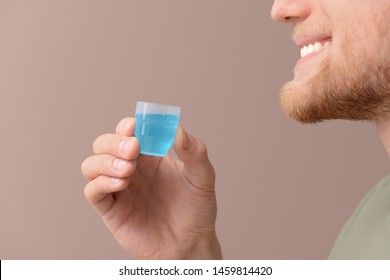 Young Man With Cup Of Mouthwash On Color Background