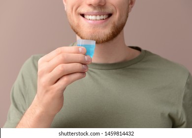 Young Man With Cup Of Mouthwash On Color Background