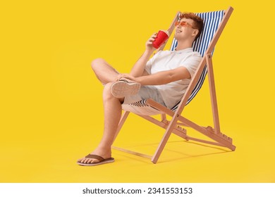 Hombre joven con taza de refresco descansando en una tumbona de fondo amarillo