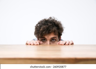 Young man with curly hair peeking from behind the desk