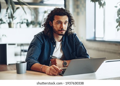 Young man with curly hair sitting at his workplace with laptop