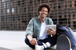 Young Man With Curly Hair Using Digital Tablet. Man Sitting Outside Taking A Break