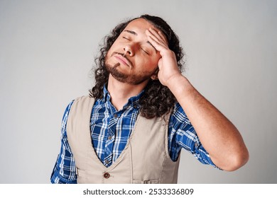 Young man with curly hair wears a plaid shirt and vest, showing signs of frustration in a studio - Powered by Shutterstock