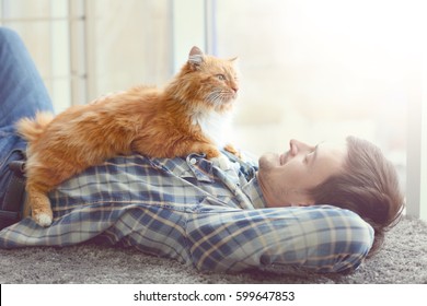 Young man with cute cat lying on floor near window