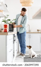 Young Man With Cute Dog Adjusting Microwave Oven In Kitchen