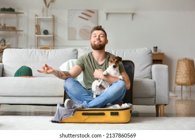 Young Man With Cute Dog Meditating In Suitcase At Home