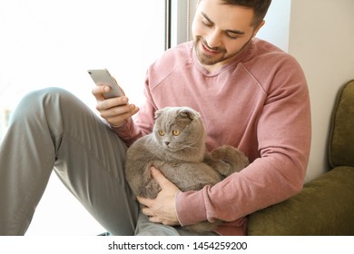 Young Man With Cute Funny Cat And Mobile Phone At Home