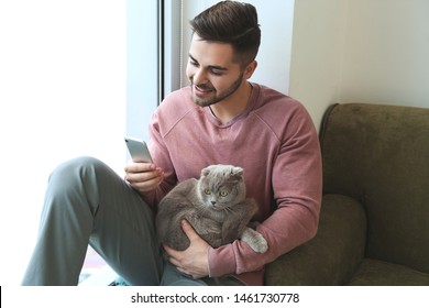 Young Man With Cute Funny Cat And Mobile Phone At Home