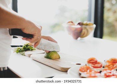 Young man cutting avocado and making toasts with tomato, arugula, cheese in modern white kitchen. Healthy eating and Home cooking concept. Perfectly ripe avocado in hands - Powered by Shutterstock