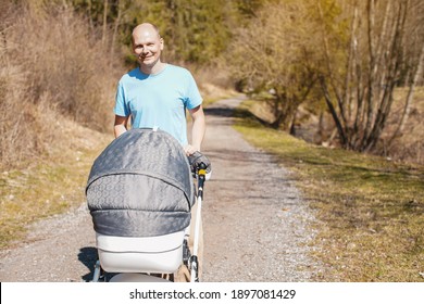 Young Man In Cyan T Shirt Pushing Baby Carriage On Forest Road In Spring