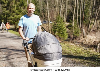 Young Man In Cyan T Shirt Pushing Baby Carriage On Forest Road In Spring