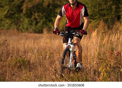 Young man cycling on a rural road through in the autumn forest during sunset - Shutterstock ID 351810608