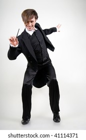 A young man dancing in a black tailcoat is pointing the stick to the camera and smiling