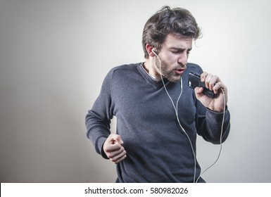 Young Man Dancing And Singing To The Music On His Mobile Phone Through Earphones, Goofy And Happy