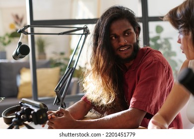 Young Man With Dark Long Thick Hair Looking At Girl During Discussion Of Popular Topic In Studio While Making Record Of Their Talk