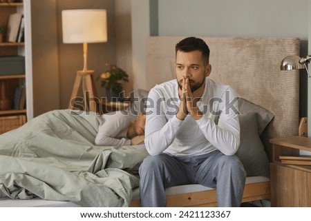 Young man deep in thoughts while his wife sleeps in the background