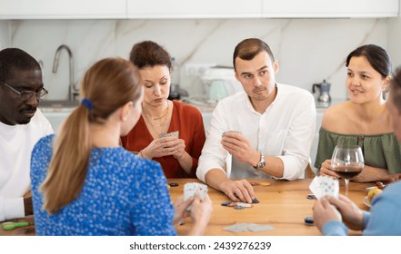 Young man deeply engrossed in friendly poker game with group of friends of different nationalities in relaxed home atmosphere around kitchen table.. - Powered by Shutterstock