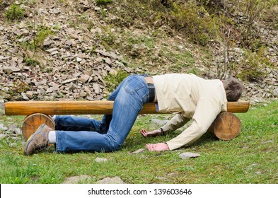 Young man deeply sleeping or drunk, laying outdoors on a wooden park bench. Profile view
